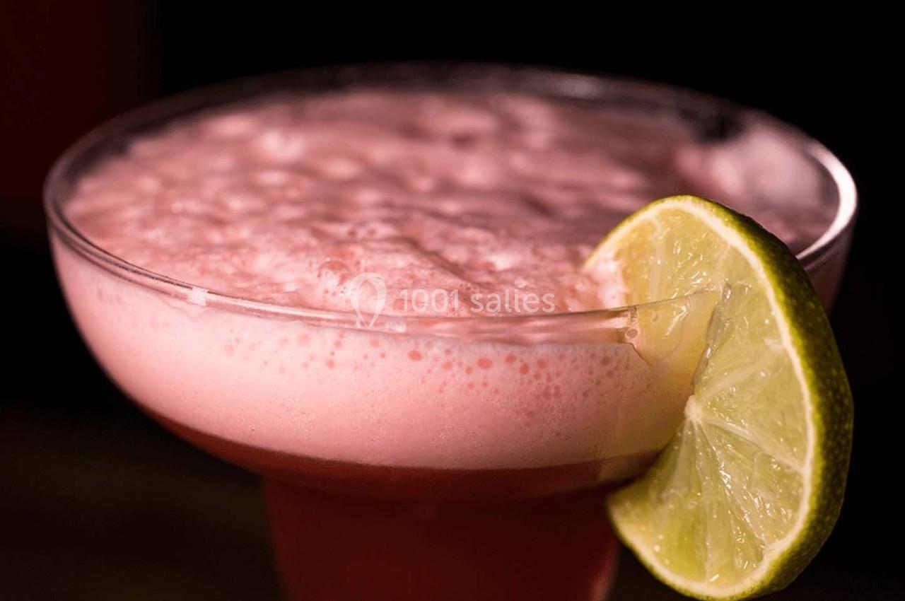 Cocktail rose mousseux servi dans un verre à pied, garni d'une tranche de citron vert.