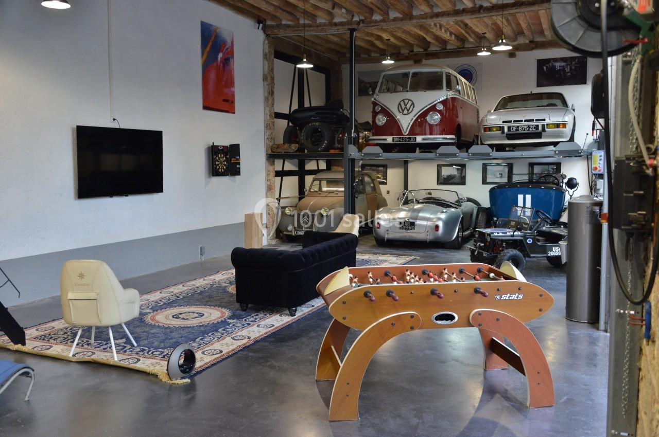 Salle aménagée avec des voitures anciennes, un baby-foot, un canapé et des éléments de décoration rétro.
