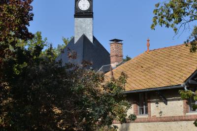 Clocher d'église avec horloge visible, entouré de bâtiments en briques et de végétation sous un ciel bleu.