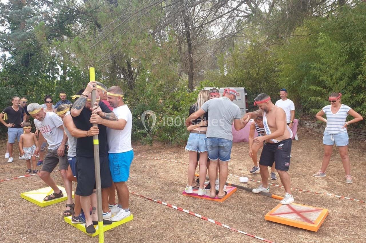 Des personnes participent à un jeu d'équipe en extérieur, debout sur des plateformes colorées, entourées de végétation.