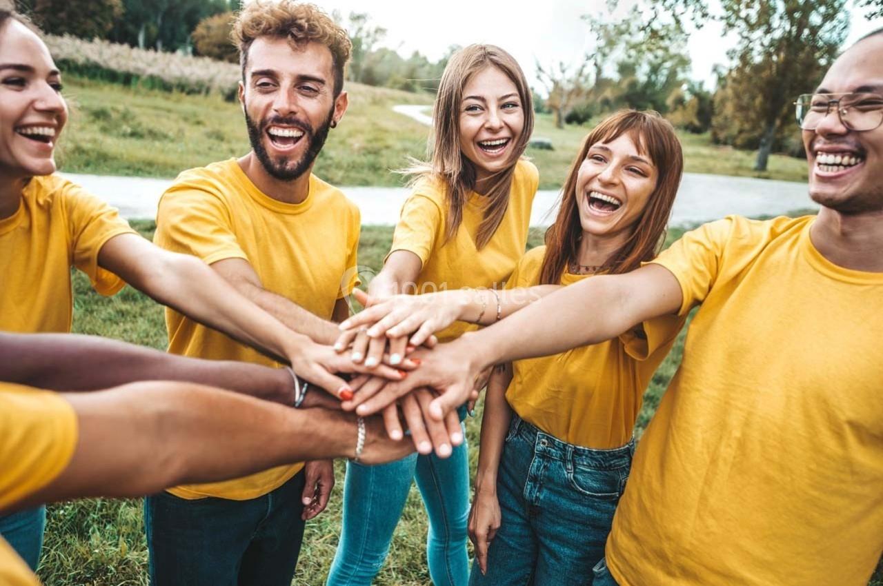 Un groupe de personnes souriantes en t-shirts jaunes joignant leurs mains au centre dans un parc verdoyant.