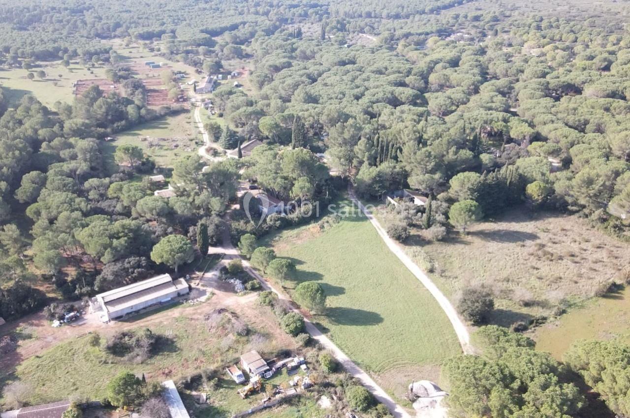 Vue aérienne d'une zone rurale avec des bâtiments dispersés, des chemins et une forêt de pins environnante.