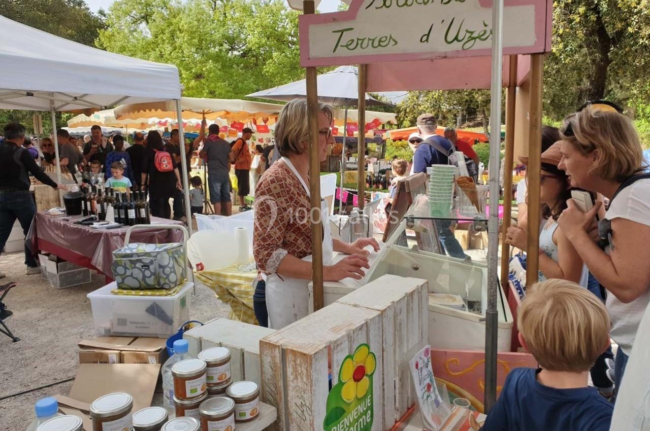 Stand de produits bio dans un marché en plein air, avec des clients discutant et des étals colorés en arrière-plan.