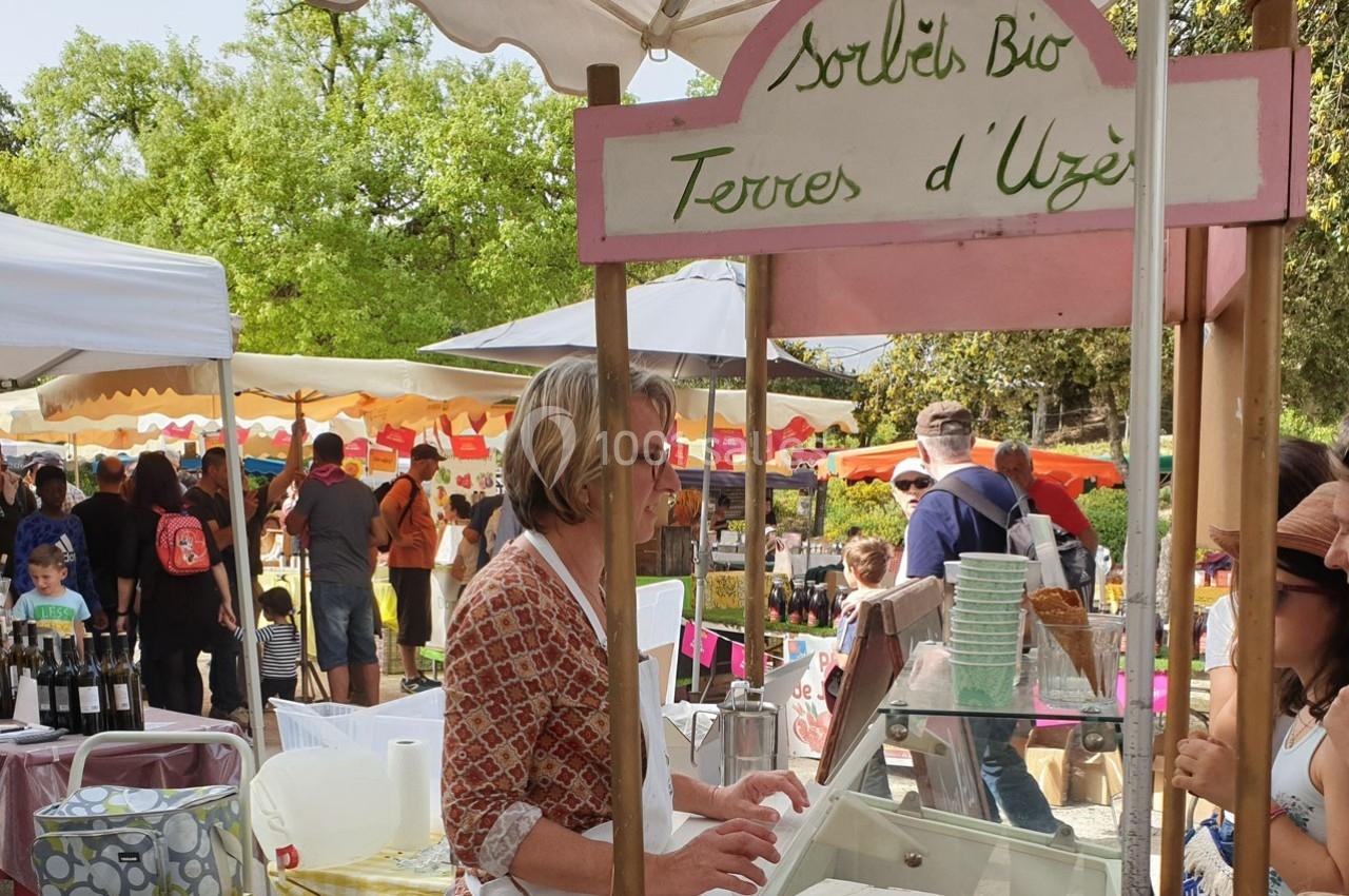 Une vendeuse sert des glaces artisanales sous un stand au marché en plein air, entourée de visiteurs.