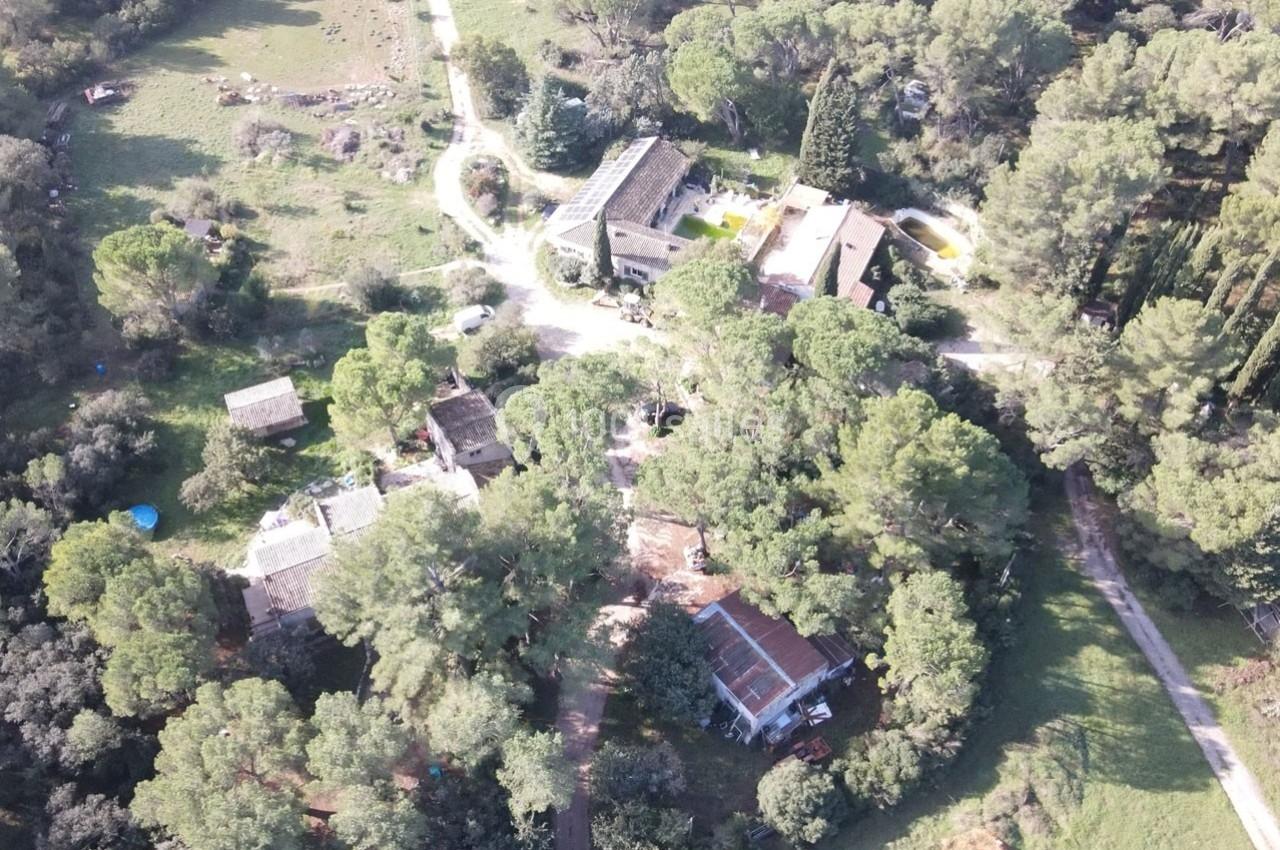 Vue aérienne d'un domaine rural entouré de végétation, avec plusieurs bâtiments dispersés parmi les arbres.