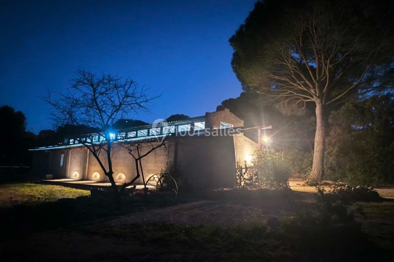 Maison moderne éclairée la nuit, entourée d'arbres et située dans un environnement naturel.