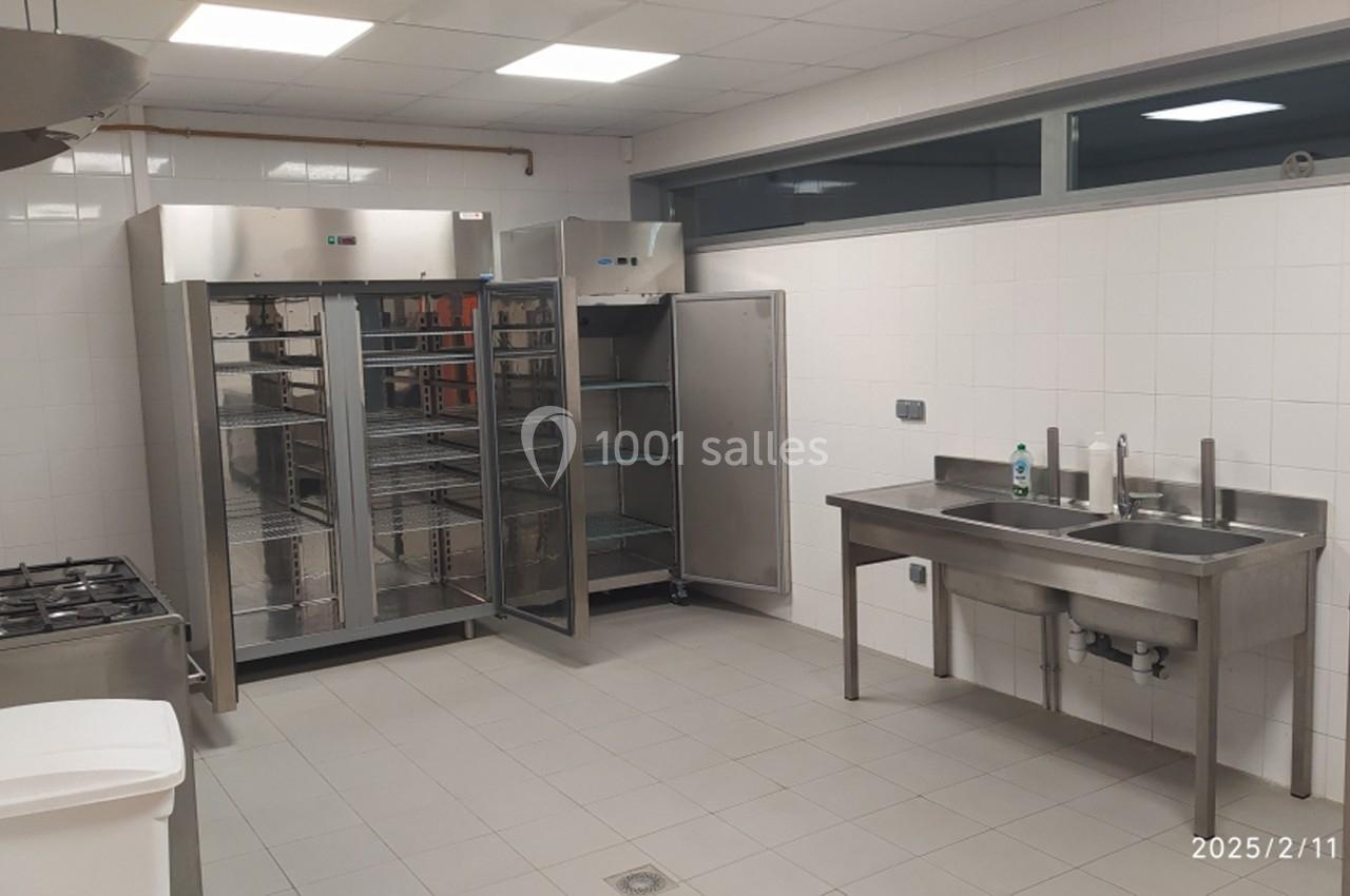 Cuisine professionnelle avec équipements en inox, incluant réfrigérateurs ouverts, évier double et cuisinière.