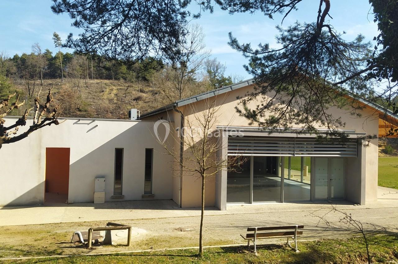 Bâtiment moderne avec façade beige, grandes baies vitrées et environnement arboré en arrière-plan.