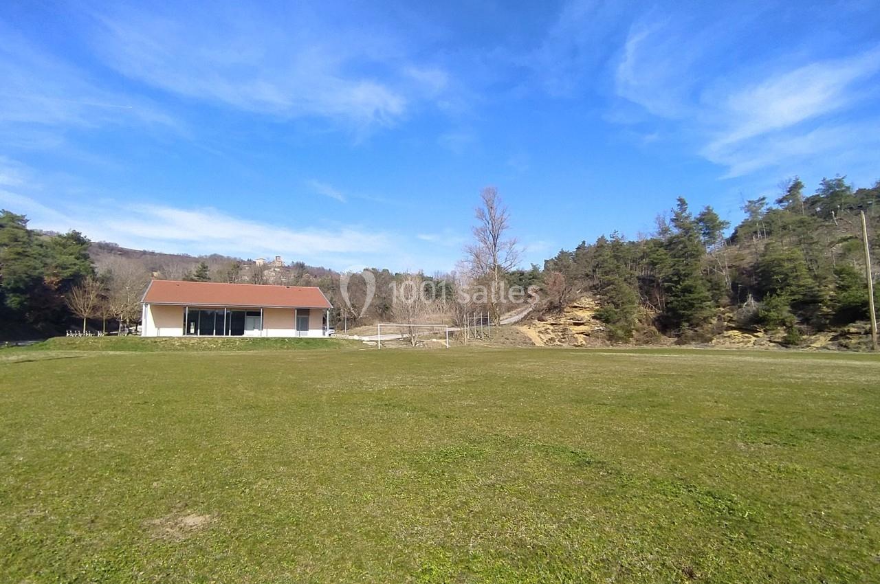 Maison blanche avec toit rouge entourée de pelouse, située près d'une forêt sous un ciel bleu dégagé.
