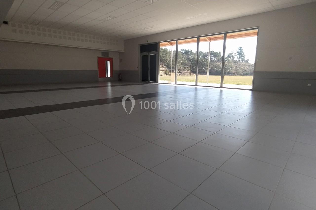 Salle vide avec carrelage clair, grande baie vitrée laissant entrer la lumière et vue sur un espace extérieur arboré.