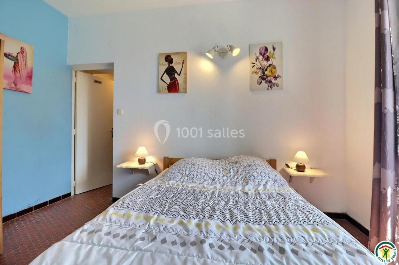 Lit double avec couvre-lit à motifs dans une chambre lumineuse, décorée de tableaux et éclairée par des lampes de chevet.