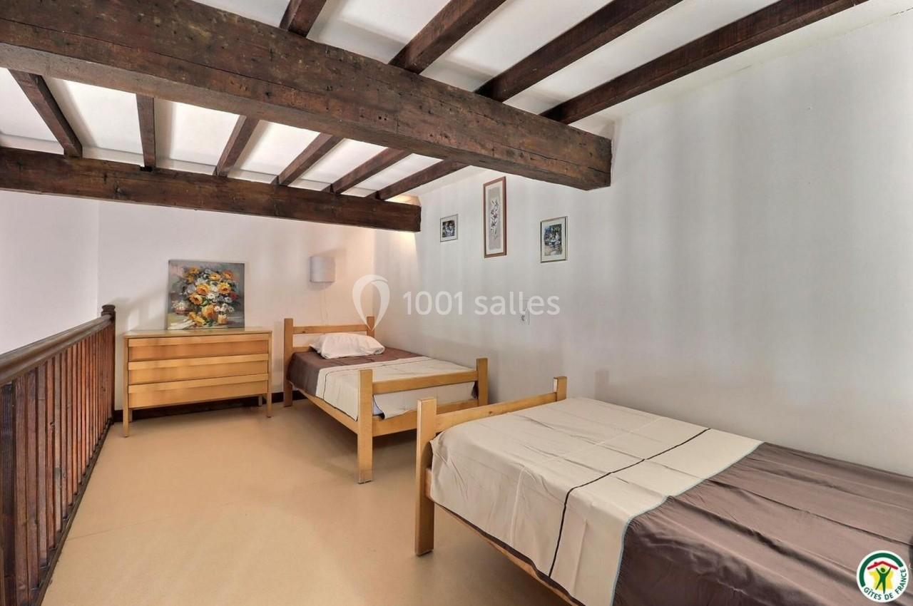 Deux lits simples en bois dans une chambre avec poutres apparentes, commode et décorations murales.