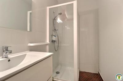 Douche moderne avec paroi vitrée, pommeau mural et lavabo blanc dans une salle de bain aux murs clairs.