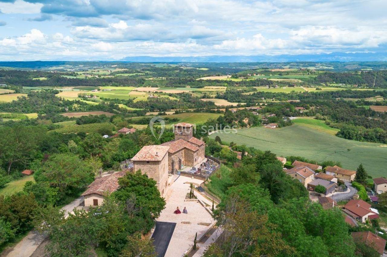 Vue aérienne d'un village rural avec une église en pierre entourée de maisons et de paysages verdoyants.