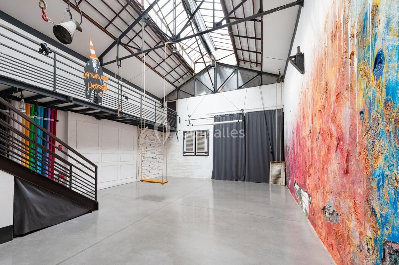 Intérieur d'un loft lumineux avec mezzanine, murs colorés et grande verrière laissant entrer la lumière naturelle.