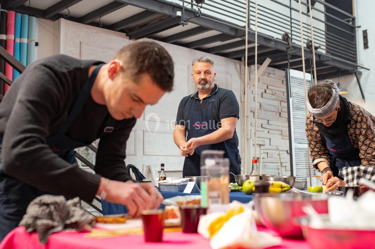 Des personnes en tablier cuisinent sur des plans de travail dans un espace lumineux et moderne.