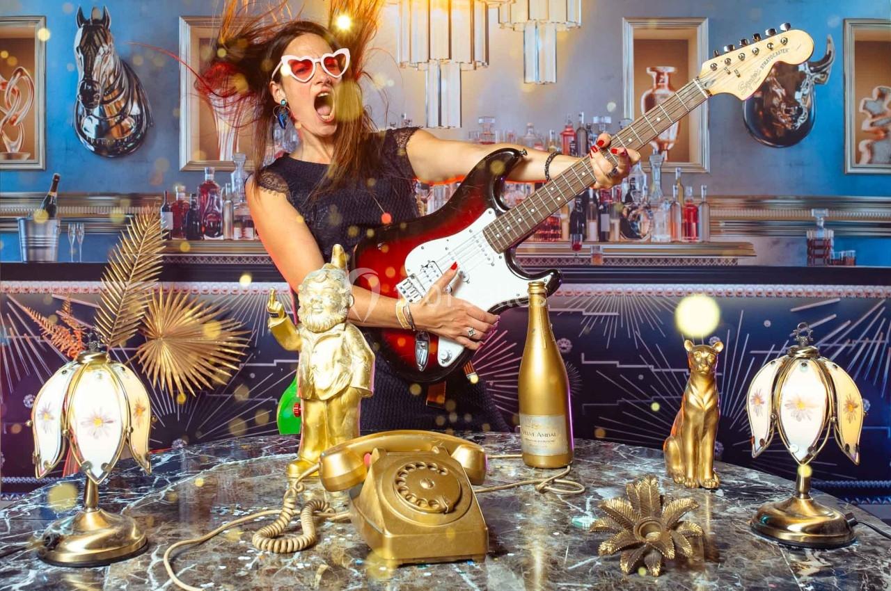 Femme jouant de la guitare électrique dans un décor rétro avec des objets dorés et un téléphone ancien sur une table en…