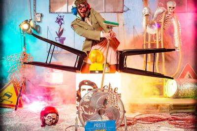 Femme portant des lunettes en forme de cœur jouant de la guitare électrique dans un décor rétro avec objets dorés.