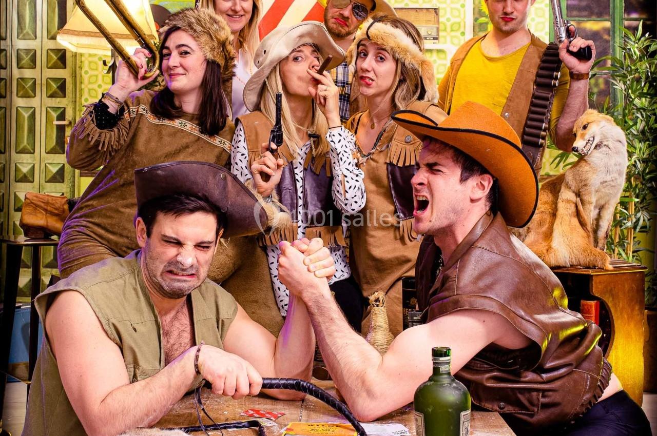 Des personnes déguisées en cowboys et cowgirls dans une scène humoristique, deux hommes font un bras de fer au premier plan.