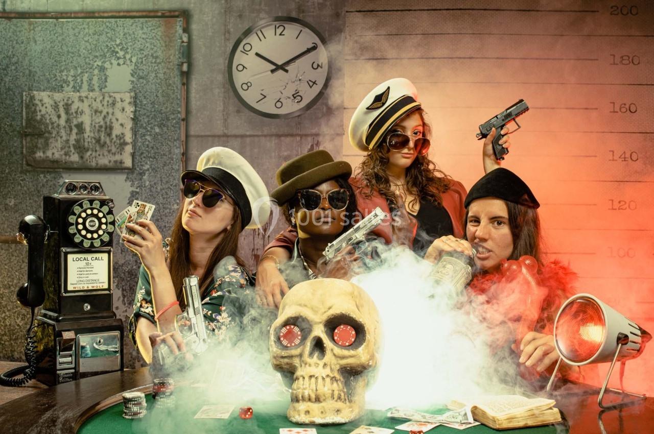 Quatre personnes déguisées autour d'une table de poker avec un crâne, des cartes, des dés et de la fumée.