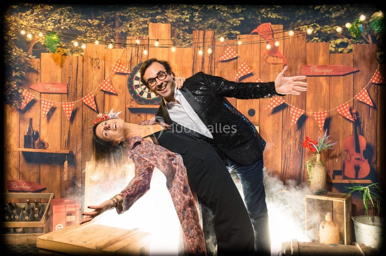 Un homme et une femme posent en dansant devant une décoration festive en bois avec guirlandes lumineuses.