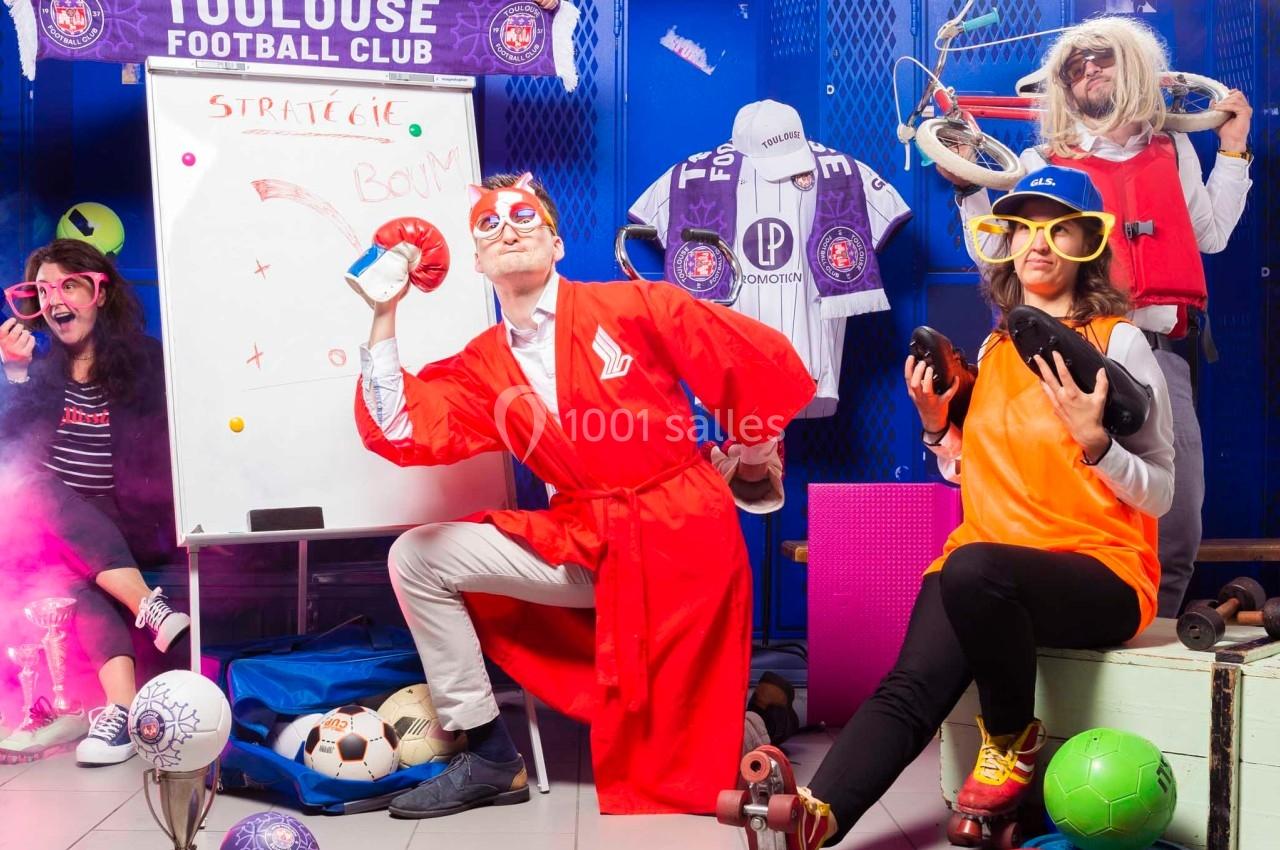 Des personnes déguisées posent dans un vestiaire de football, entourées d'accessoires sportifs et festifs.
