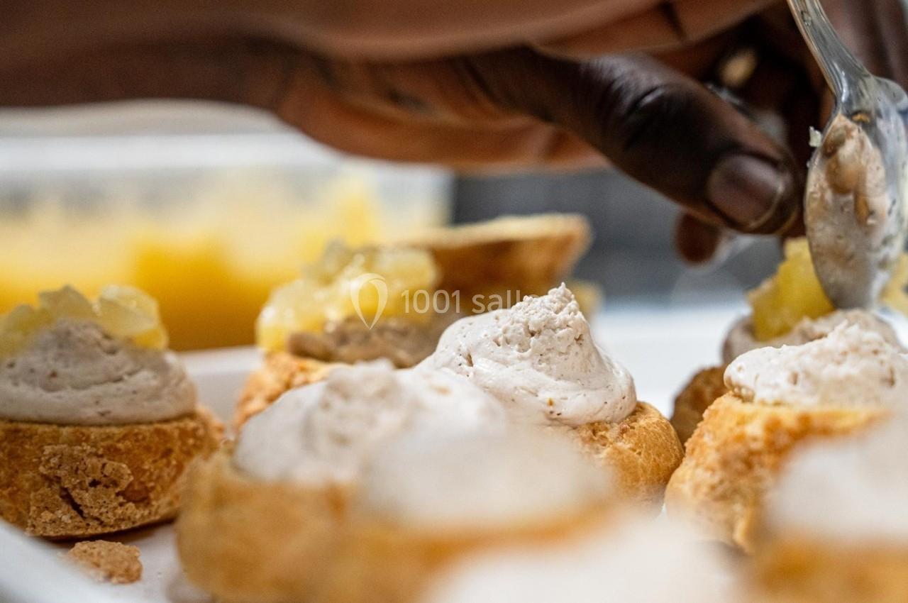 Main ajoutant une garniture à des choux à la crème sur une assiette blanche, avec un bol de garniture en arrière-plan.