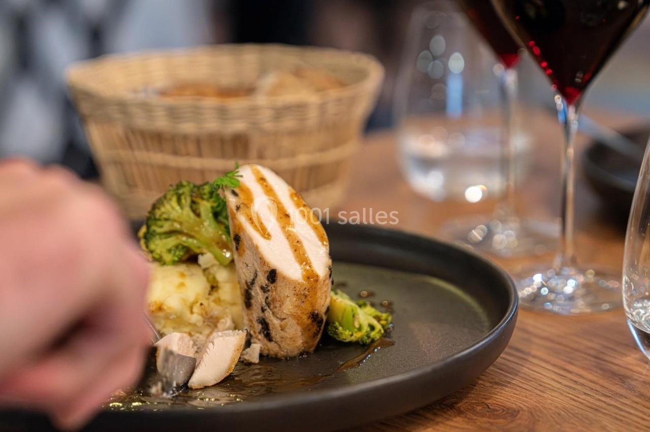 Assiette contenant du poulet grillé, purée, brocolis, avec un verre de vin rouge et une corbeille de pain en arrière-plan.