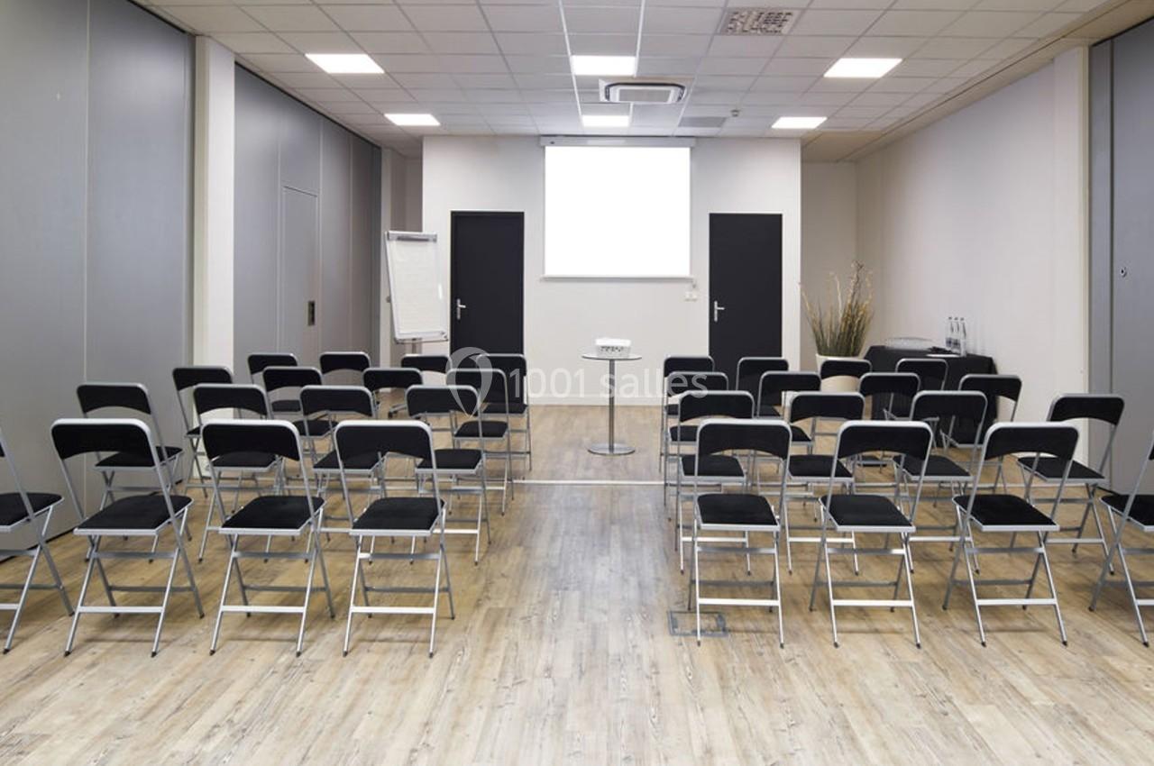 Salle de conférence vide avec des chaises noires alignées face à un écran de projection blanc.