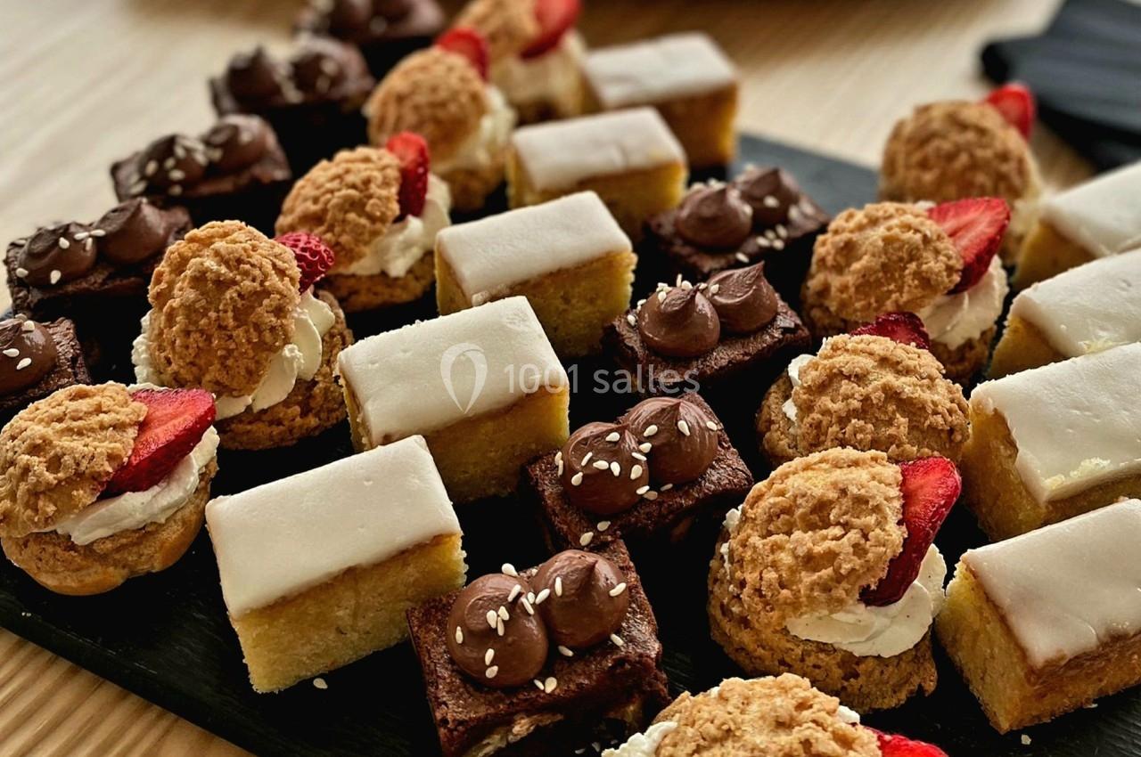 Plateau de pâtisseries variées comprenant choux, gâteaux glacés et brownies décorés, posé sur une table en bois.