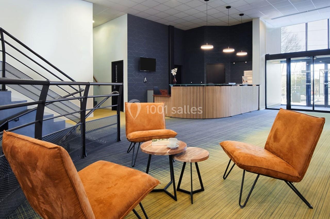 Espace d'accueil moderne avec fauteuils orange, tables basses en bois, comptoir en bois et éclairage suspendu.