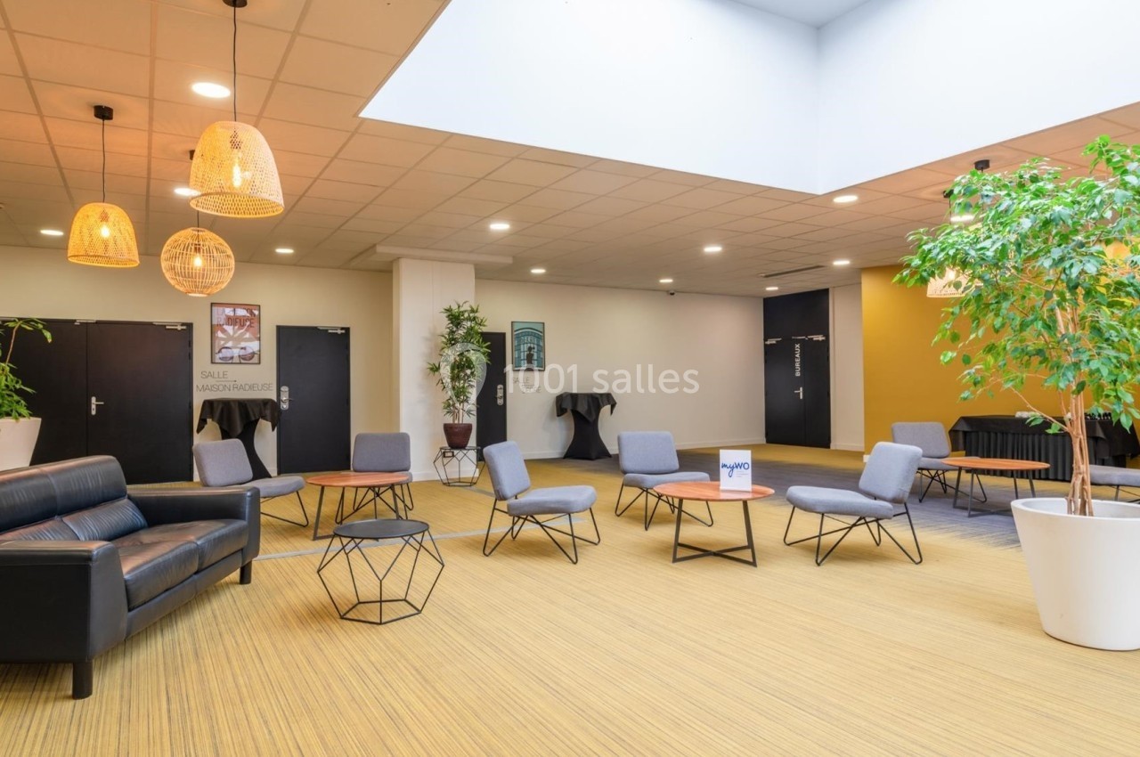 Espace d'attente lumineux avec fauteuils, tables basses, plantes en pot et suspensions en osier.