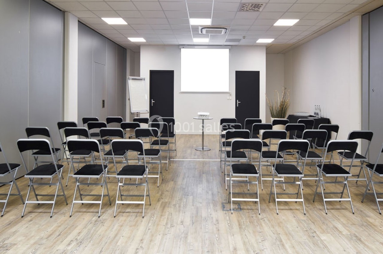 Salle de réunion avec des chaises noires alignées face à un écran de projection blanc et un pupitre central.