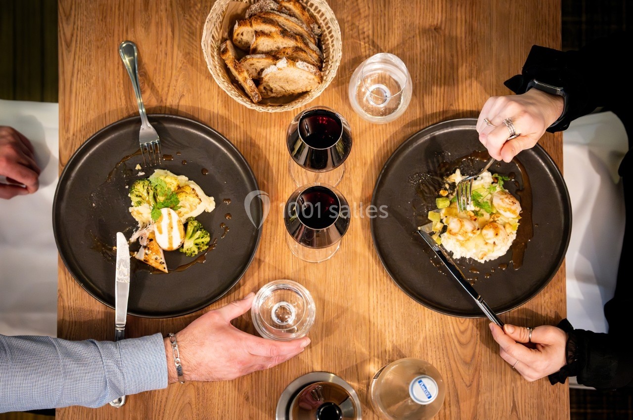 Deux assiettes garnies de plats raffinés avec du vin rouge, du pain et de l'eau sur une table en bois.