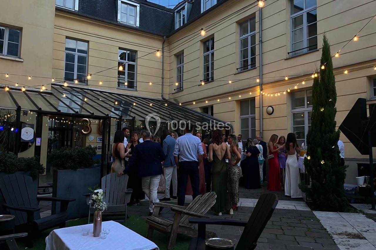 Groupe de personnes réunies dans une cour intérieure éclairée par des guirlandes lumineuses, ambiance festive en soirée.