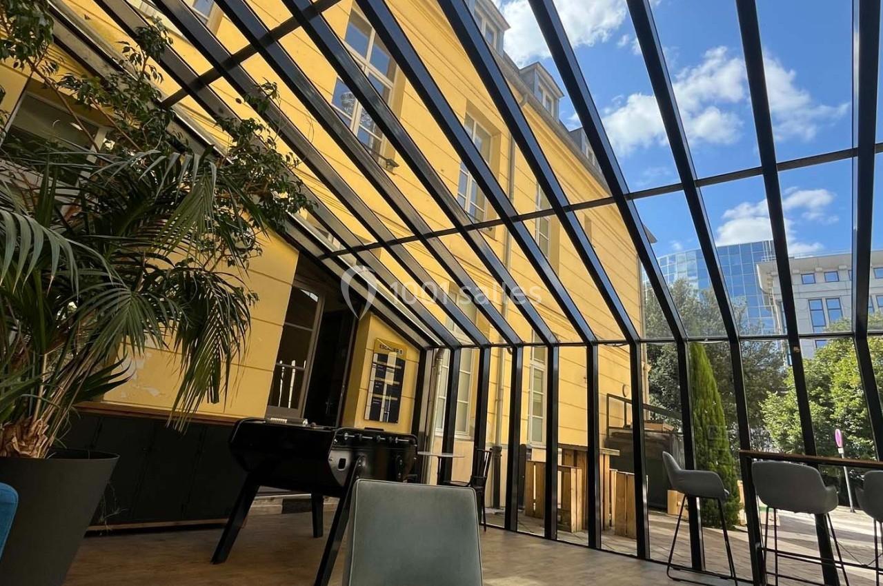 Verrière lumineuse d'un espace intérieur avec vue sur un bâtiment jaune, des plantes et un baby-foot.