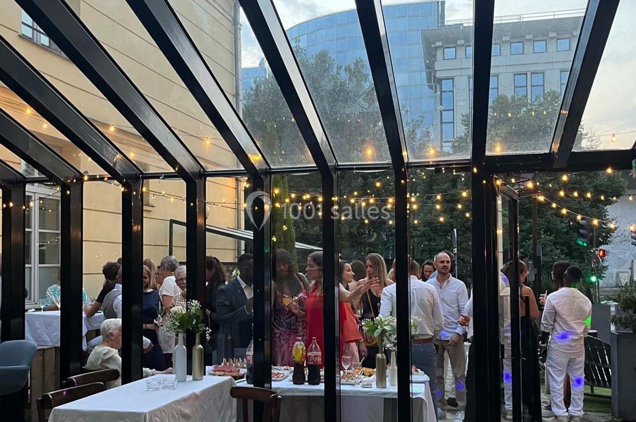 Des convives discutent et partagent un moment convivial sous une verrière décorée de guirlandes lumineuses.