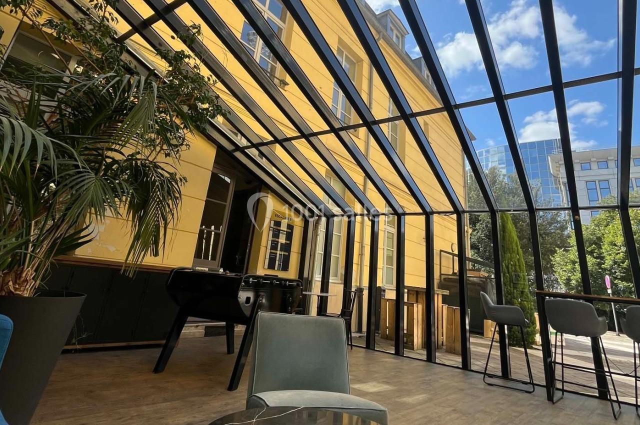 Verrière lumineuse donnant sur une terrasse avec mobilier moderne, plantes et vue sur des bâtiments environnants.