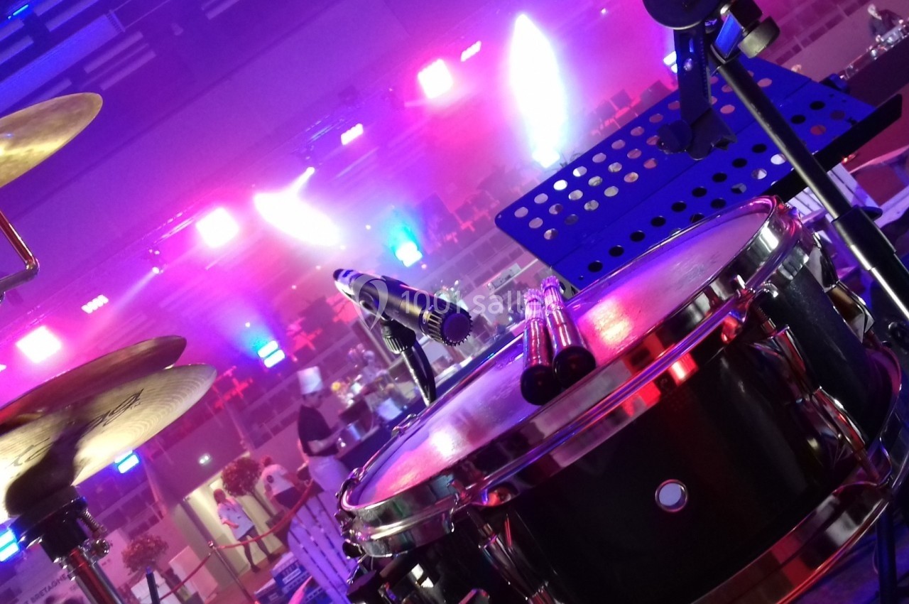 Batterie installée sur une scène éclairée par des lumières colorées, avec un pupitre en arrière-plan.