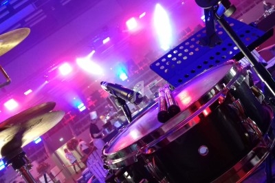 Batterie en gros plan sur une scène éclairée par des lumières colorées, avec un pupitre en arrière-plan.