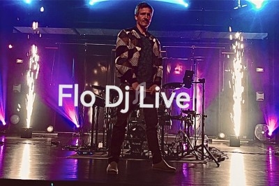 Homme debout sur une scène éclairée avec des effets lumineux et des étincelles, devant une batterie.