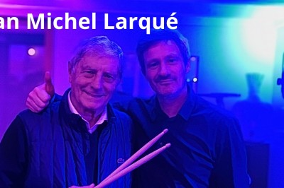 Homme en chemise noire, lunettes de soleil, fumant un cigare, tenant un verre devant un bar rempli de bouteilles.