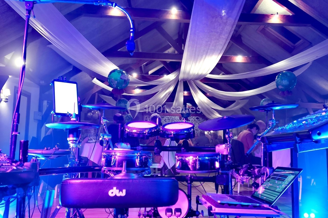 Batterie électronique et équipements audio installés dans une salle éclairée par des lumières colorées et des voilages…