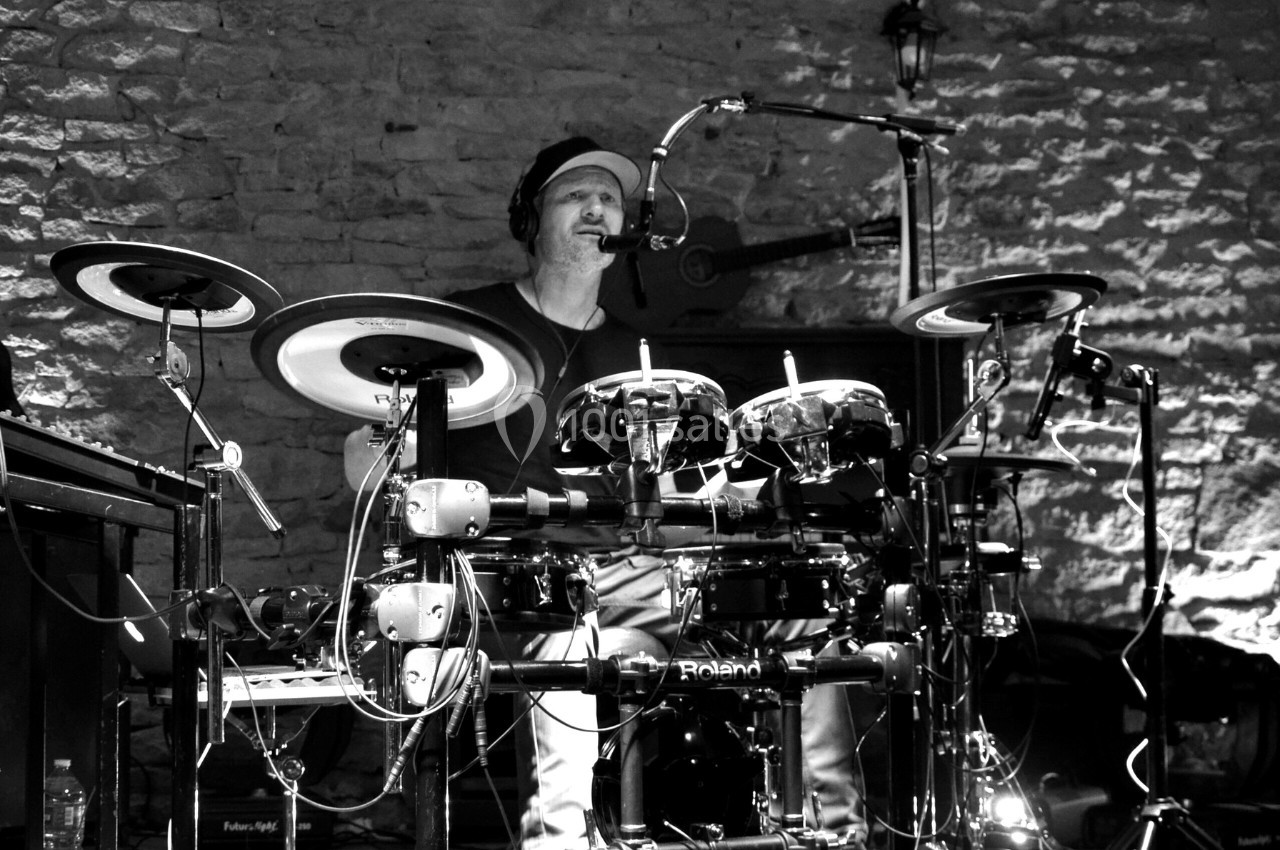 Un musicien joue de la batterie électronique dans un cadre en pierre, avec un micro et un éclairage tamisé.