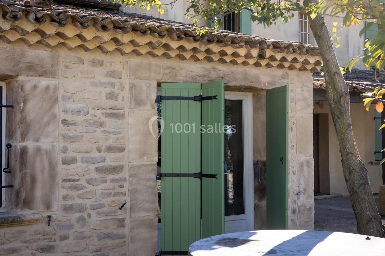 Façade en pierre d'une maison avec des volets verts ouverts et un arbre à proximité.