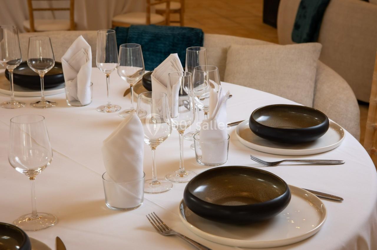 Table dressée avec nappes blanches, assiettes noires, verres à pied et serviettes pliées.