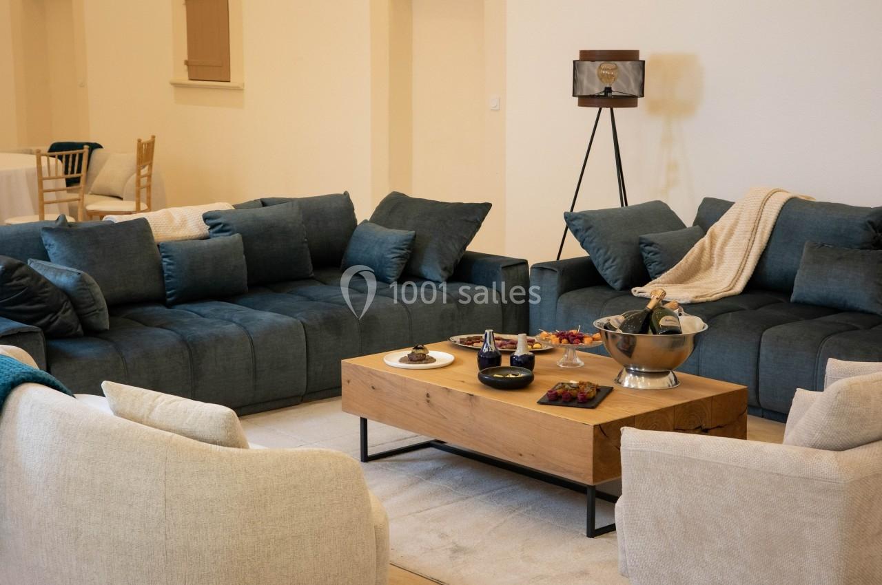 Salon avec deux canapés bleu foncé, deux fauteuils beiges, une table basse en bois et des collations disposées dessus.
