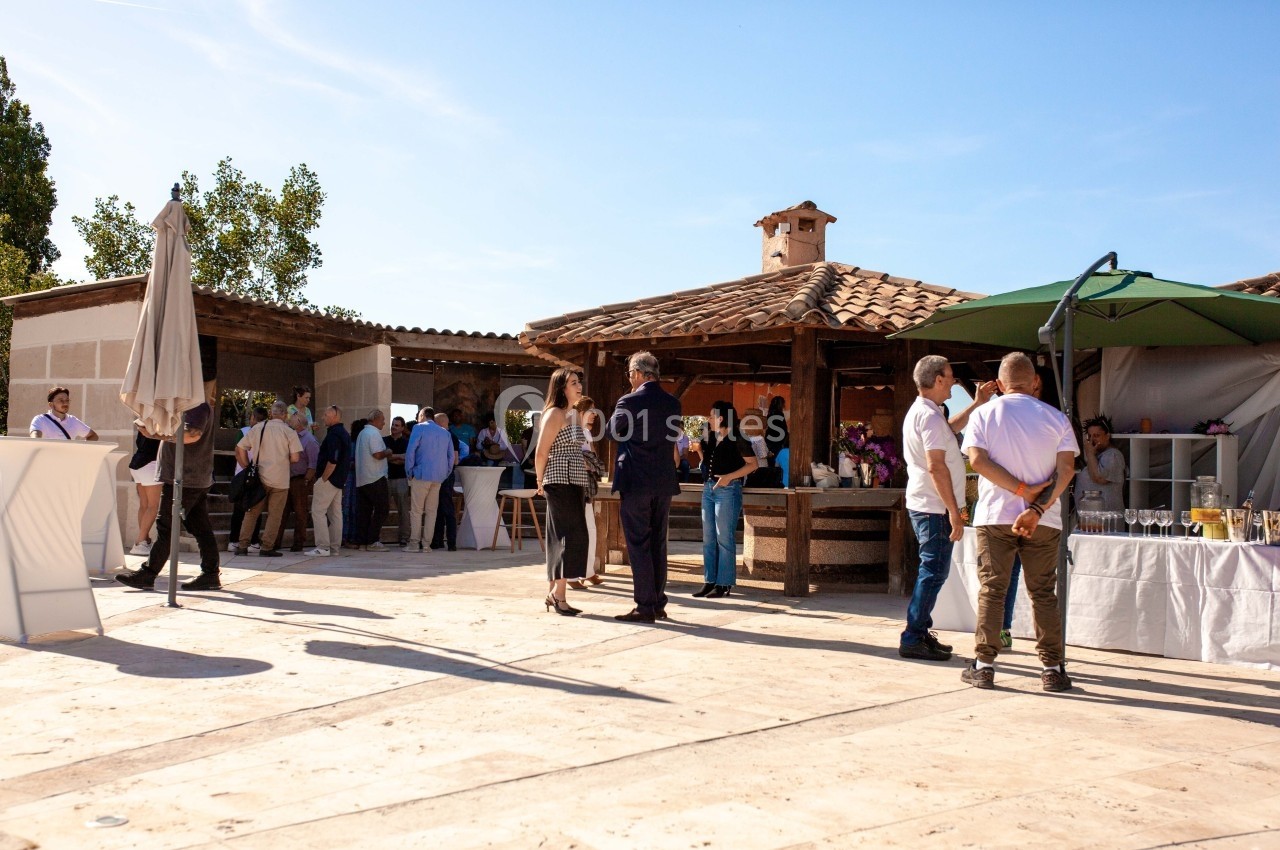 Des personnes discutent et se restaurent dans une cour ensoleillée avec des stands et des parasols.