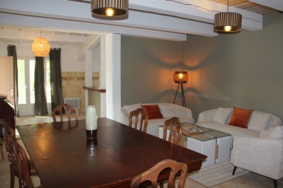 Salle à manger et salon avec table en bois, canapés clairs, lampes suspendues et lumière naturelle.