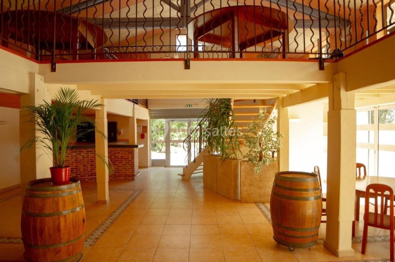 Intérieur lumineux avec mezzanine, plantes, tonneaux en bois et mobilier en bois dans un espace ouvert.
